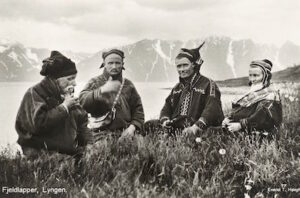 Fjällsamer i Lyngen i Troms fylke 1928. Två av männen bär den för Kautokeinoområdet så typiska "de fyra vindarnas mössa". Vykort publicerat av T. Høegh. (Wikimedia Commons)